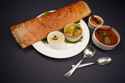 pexels-photo-20422129-20422129 Crispy dosa served with coconut chutney, vegetable curry, and sambar on a black background.